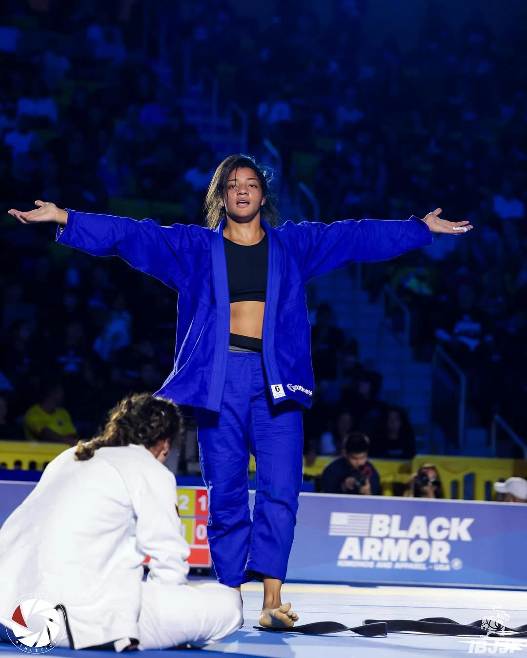 LARISSA_DIAS stands with arms outstretched on a competition ring